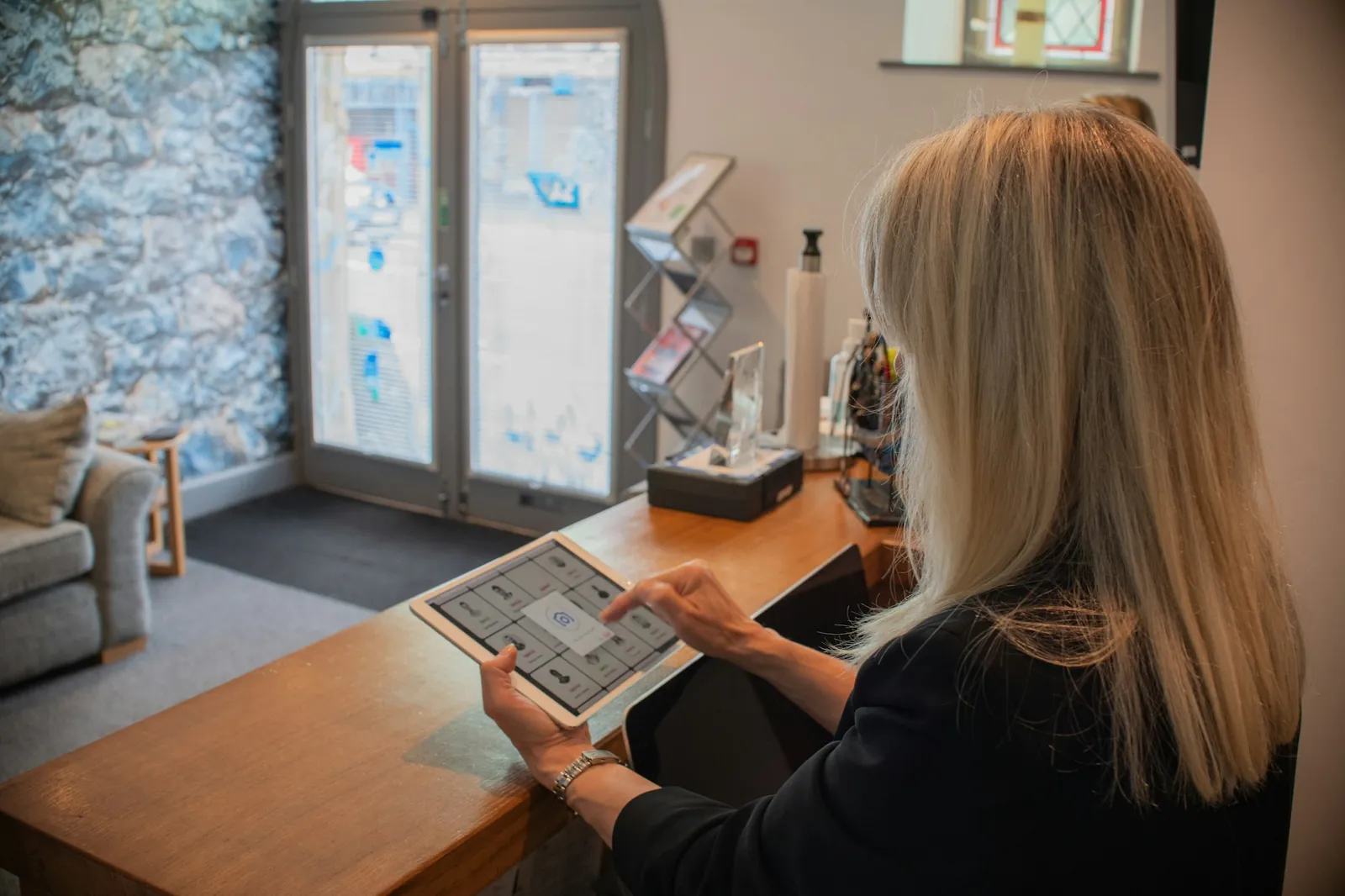 Clinic receptionist at a calm front desk confirming an appointment while a patient waits in a bright reception area